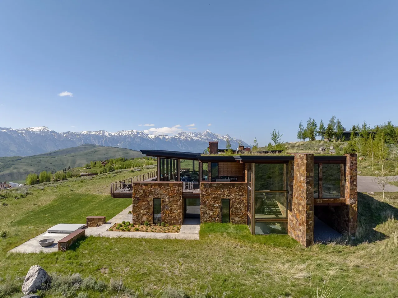 Exterior front view of a modern stone and glass house on a hillside with mountain views.