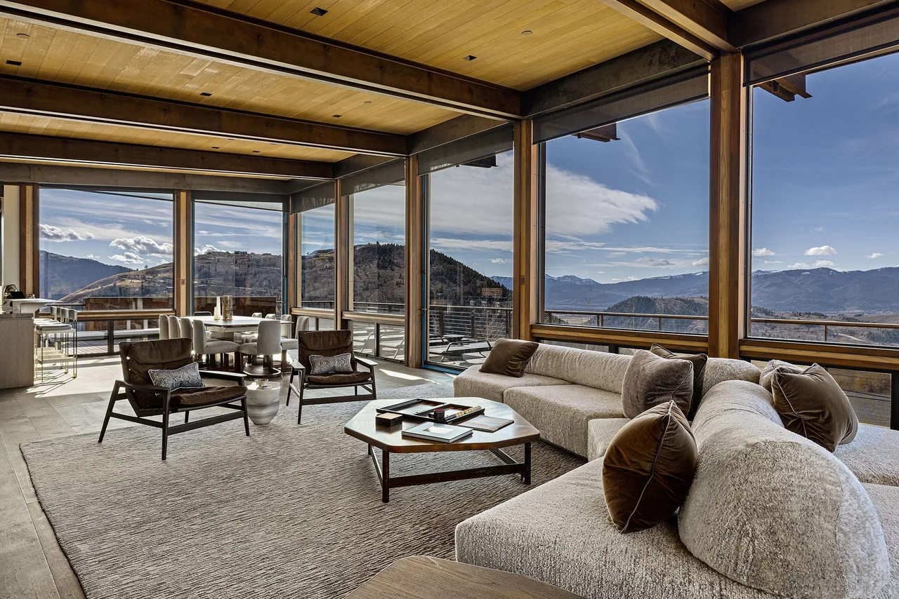 Living room with floor-to-ceiling windows overlooks mountainous landscape.