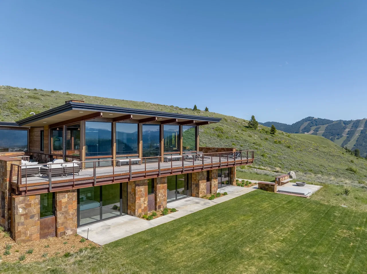 Rear exterior of a modern residence featuring extensive glazing and stone walls overlooking a hillside.