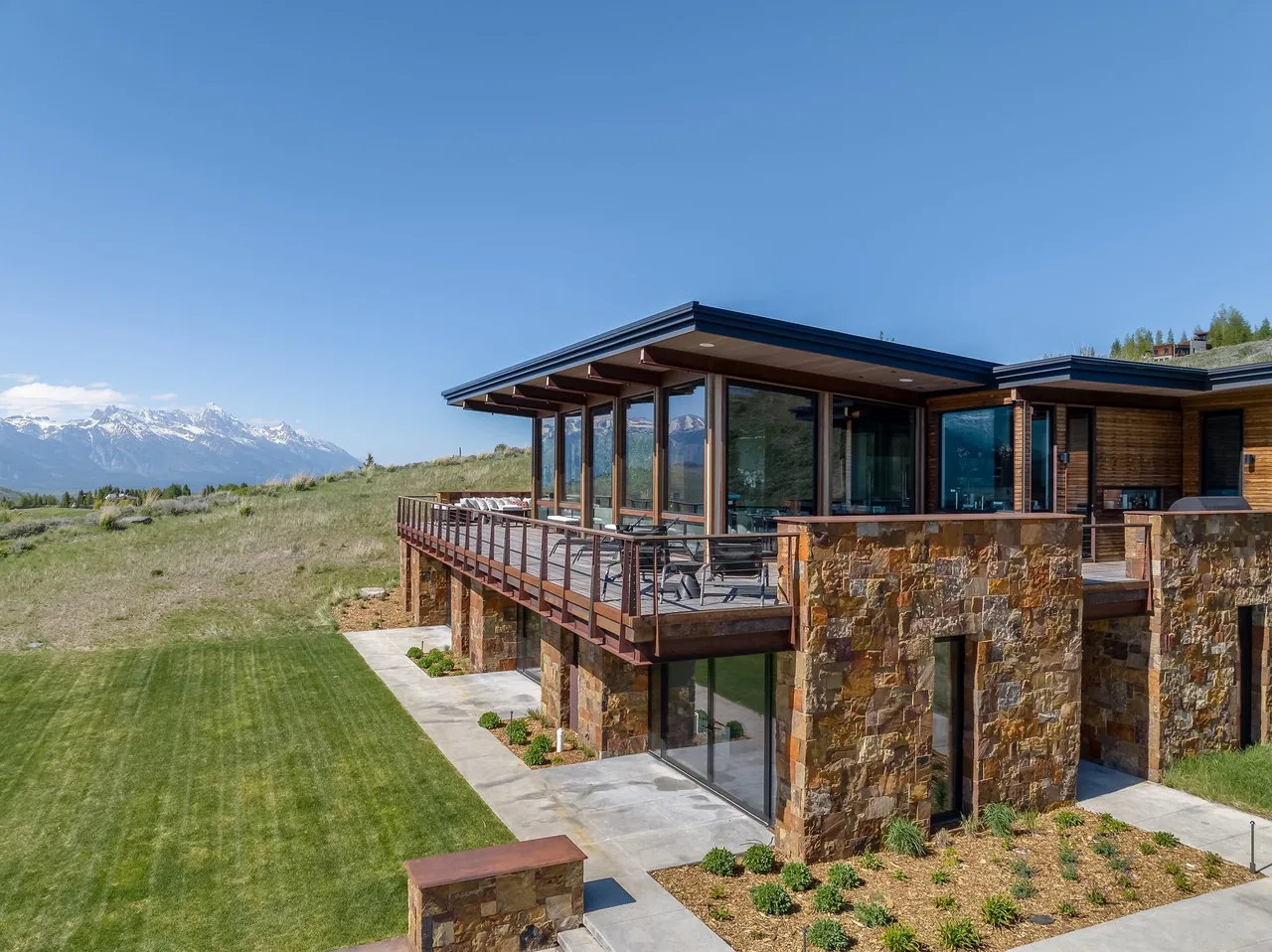 Exterior view of Ridge 52 Residence featuring stone walls, floor-to-ceiling glazing, and an elevated deck.