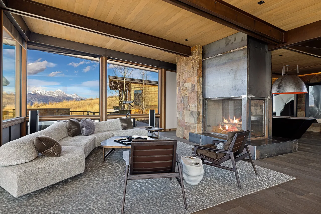 Living room featuring a metal fireplace, curved section sofa, and floor-to-ceiling windows with mountain views.