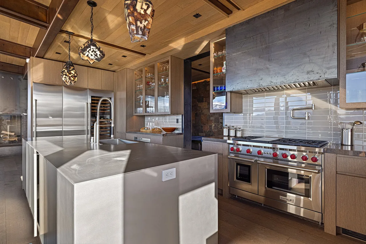 Kitchen featuring a large stainless steel island, wood cabinetry with glass-front upper cabinets, and a stainless steel stove with oven and range hood.