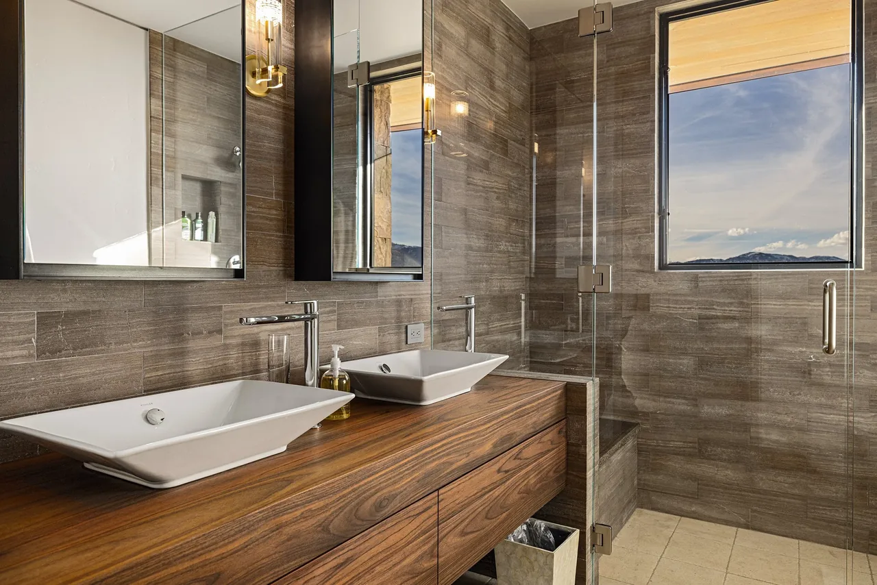 Bathroom featuring double vessel sinks, wood veneer vanity, and a walk-in shower with glass enclosure and window.