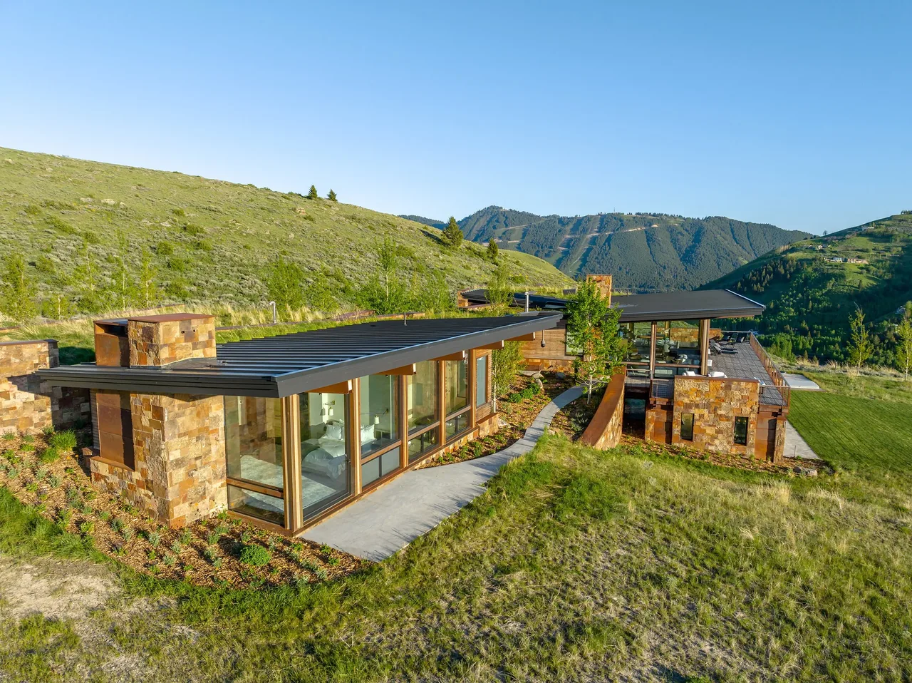 Ridge 52 Residence features stone walls with extensive floor-to-ceiling glazing and flat metal roofs on a hillside site.