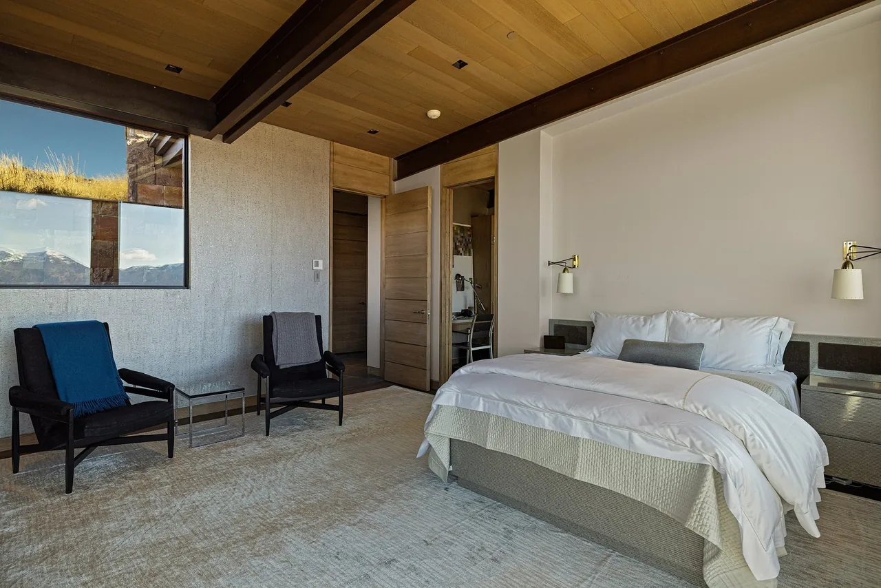 The Ridge 52 Residence bedroom features a wood-paneled ceiling, a large bed with wall sconces, and seating area with two armchairs.