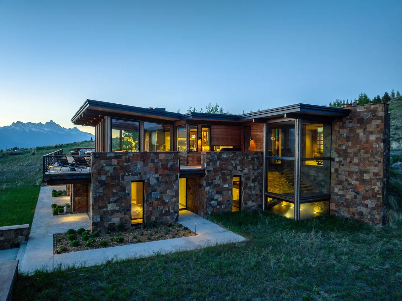 Exterior rear view of Ridge 52 Residence showing stone cladding, wood siding, and large windows at dusk.