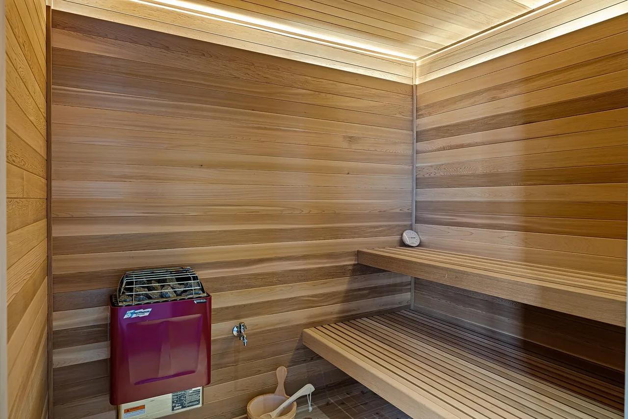 Wood-paneled sauna room featuring tiered benches and a heater with sauna stones.