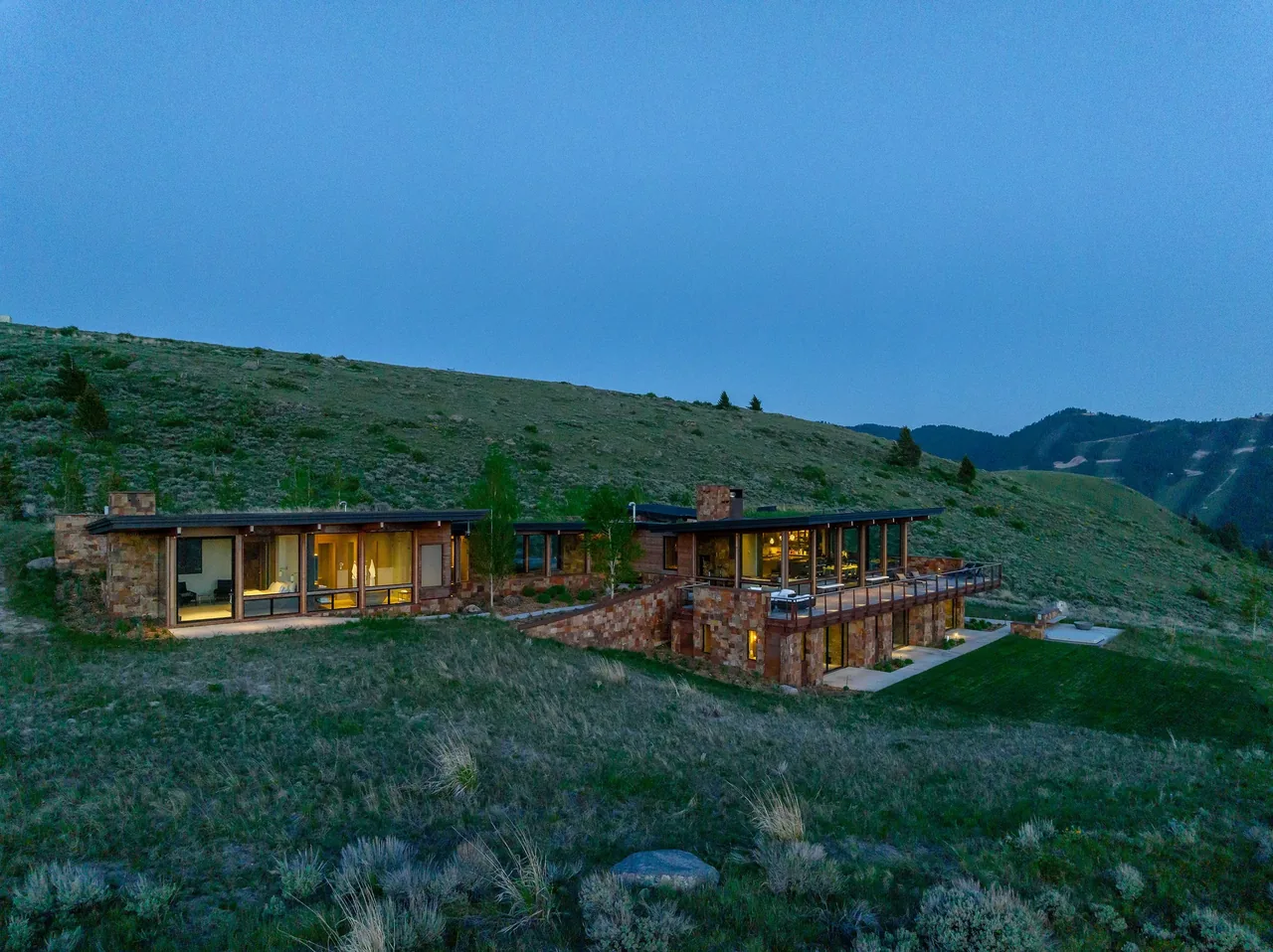 The Ridge 52 Residence features stone exterior walls and large floor-to-ceiling windows overlooking a grassy hillside.