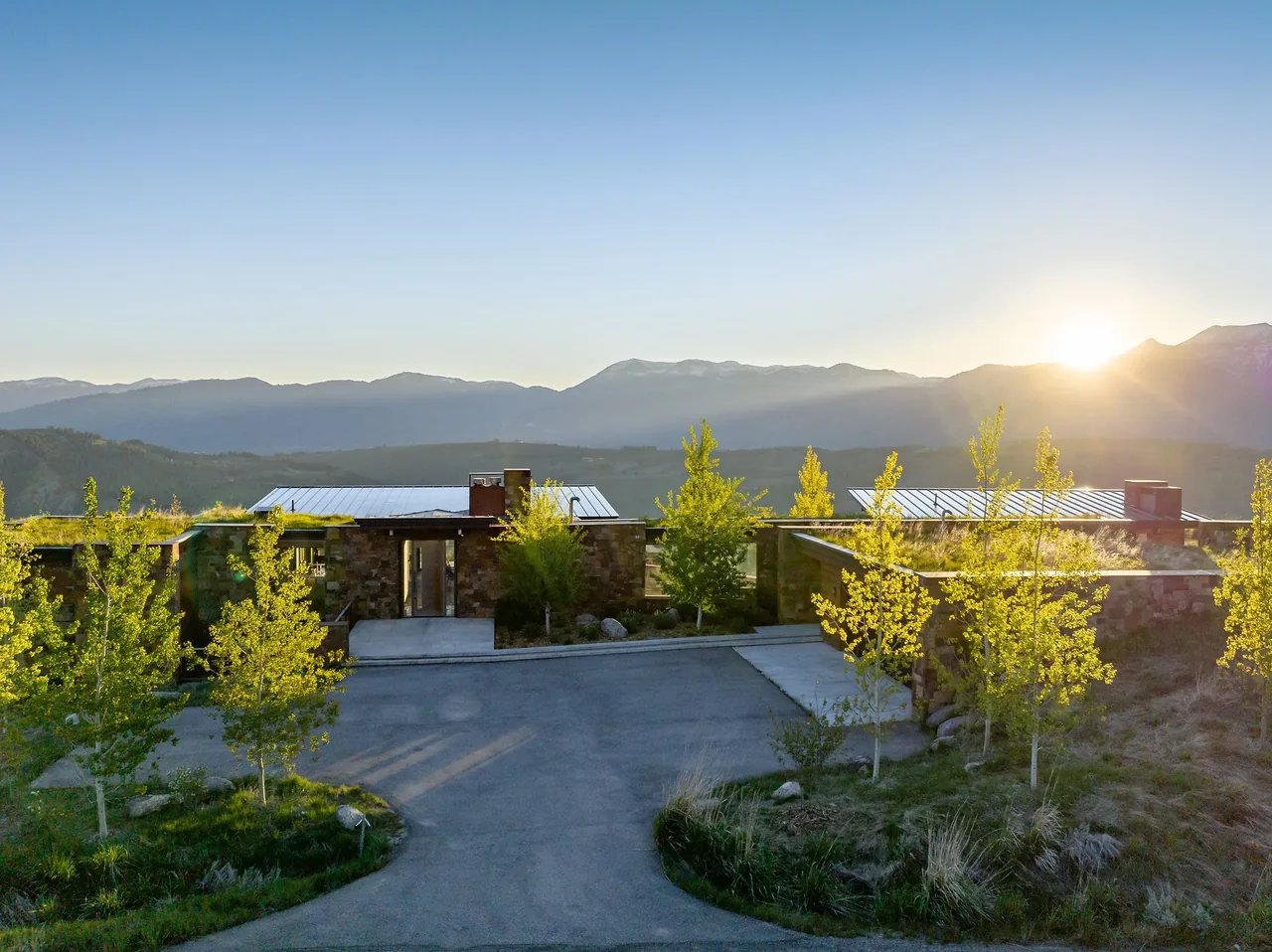 Exterior front view of the Ridge 52 Residence showing stone walls, green landscaping, and metal roofing under sunset lighting.