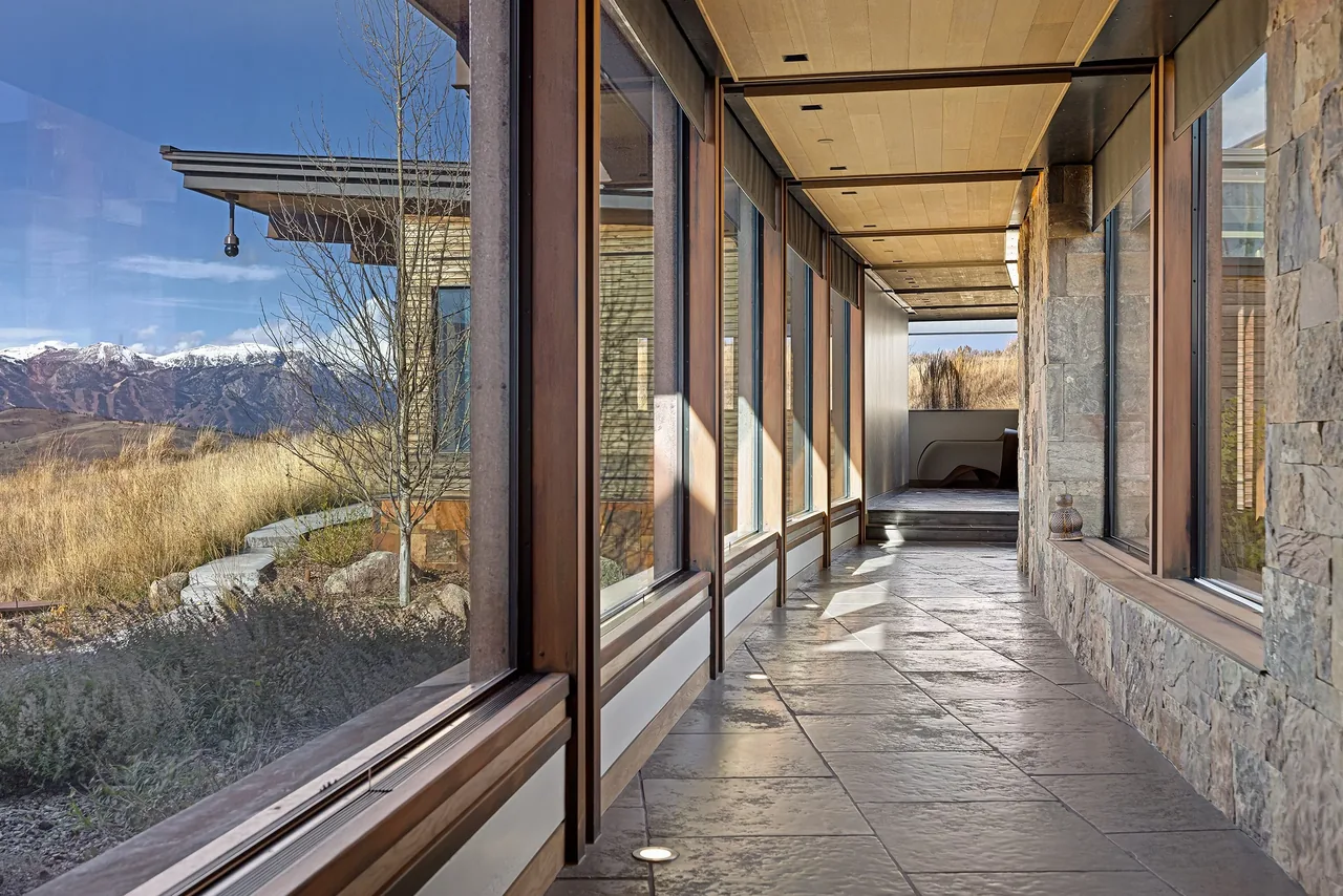Covered passageway with large windows and stone walls looking out to a mountainous landscape.