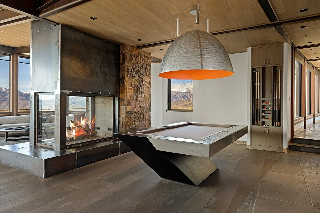 Game room interior featuring a double-sided fireplace, metallic pool table, and wood cabinetry for cue storage.