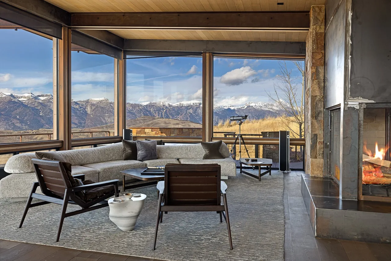 Living room with floor-to-ceiling glazing framing mountain views and a corner fireplace.