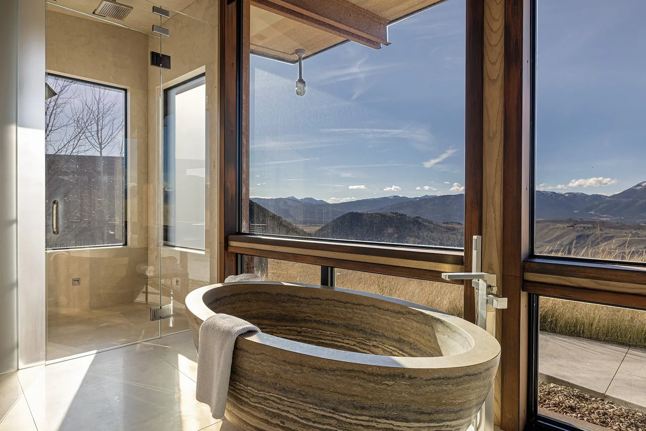 Stone freestanding tub next to large windows with mountain views in the bathroom.