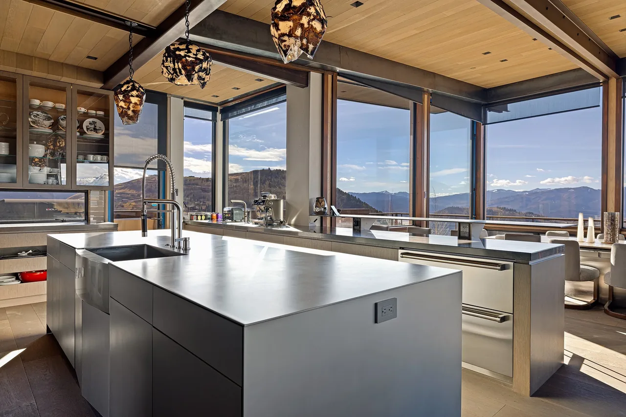 Modern kitchen with stainless steel island and expansive floor-to-ceiling windows overlooking mountainous landscape.