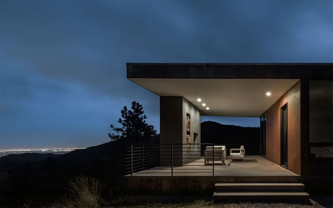 The Puma Run project by Arch 11 features a covered patio with metal railing and seating, set against a mountain view at night.
