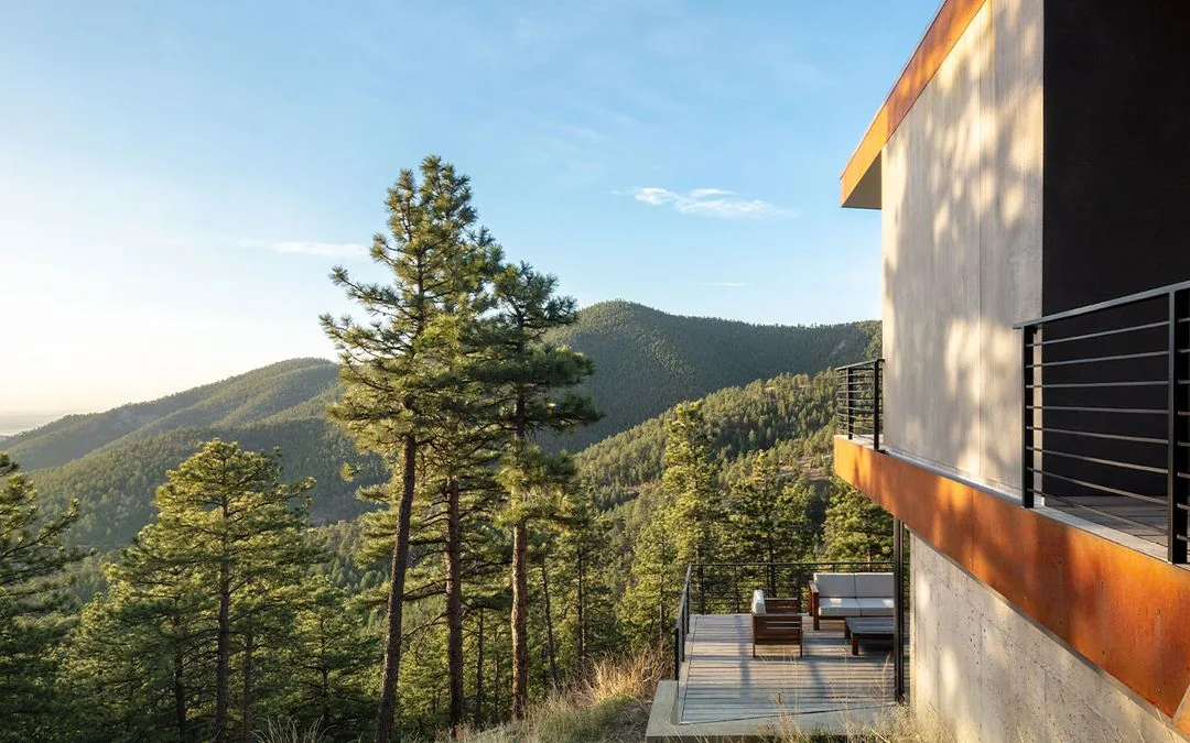 Modern covered patio with metal railing and outdoor furniture overlooking forest and mountain views.