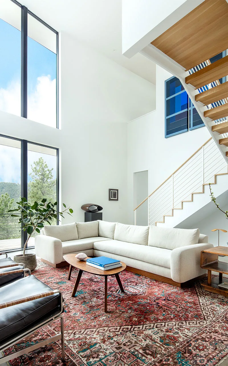 The spacious living room of Puma Run features large black-framed windows and a modern white sectional sofa with wood accents.