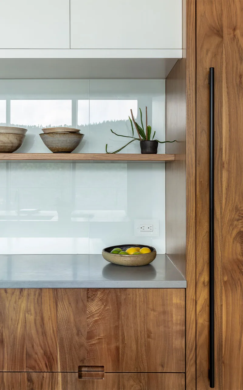 Minimalist kitchen detail with wood cabinetry, gray countertop, and ceramic bowls on a wooden shelf