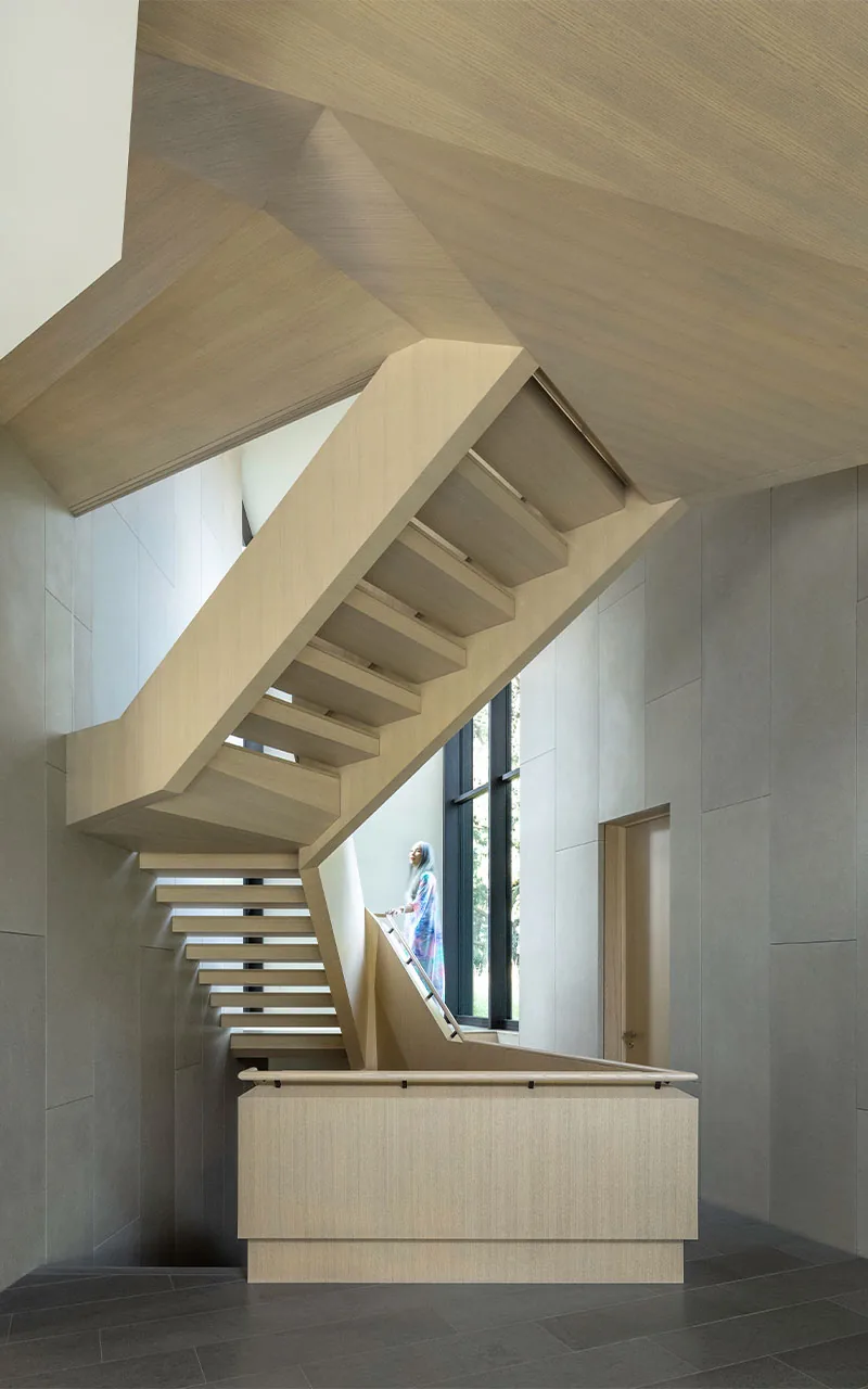 A detailed view of a light wood floating staircase with black-framed windows in a minimalist interior space.