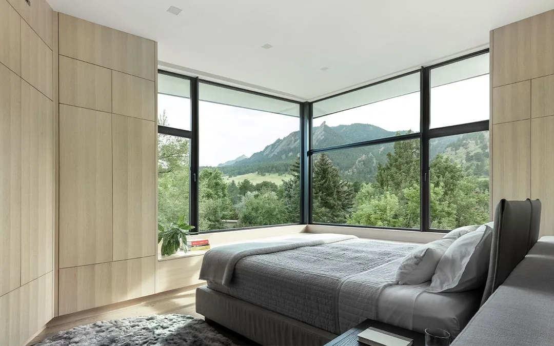 Corner bedroom with large floor-to-ceiling glazing offering views of trees and mountains.