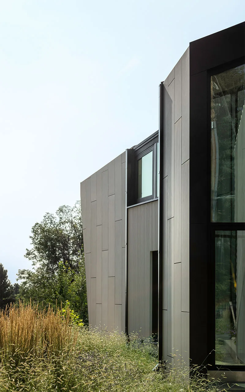 Side elevation of the Vergence House showing dark panel cladding, vertical siding, and a large window.