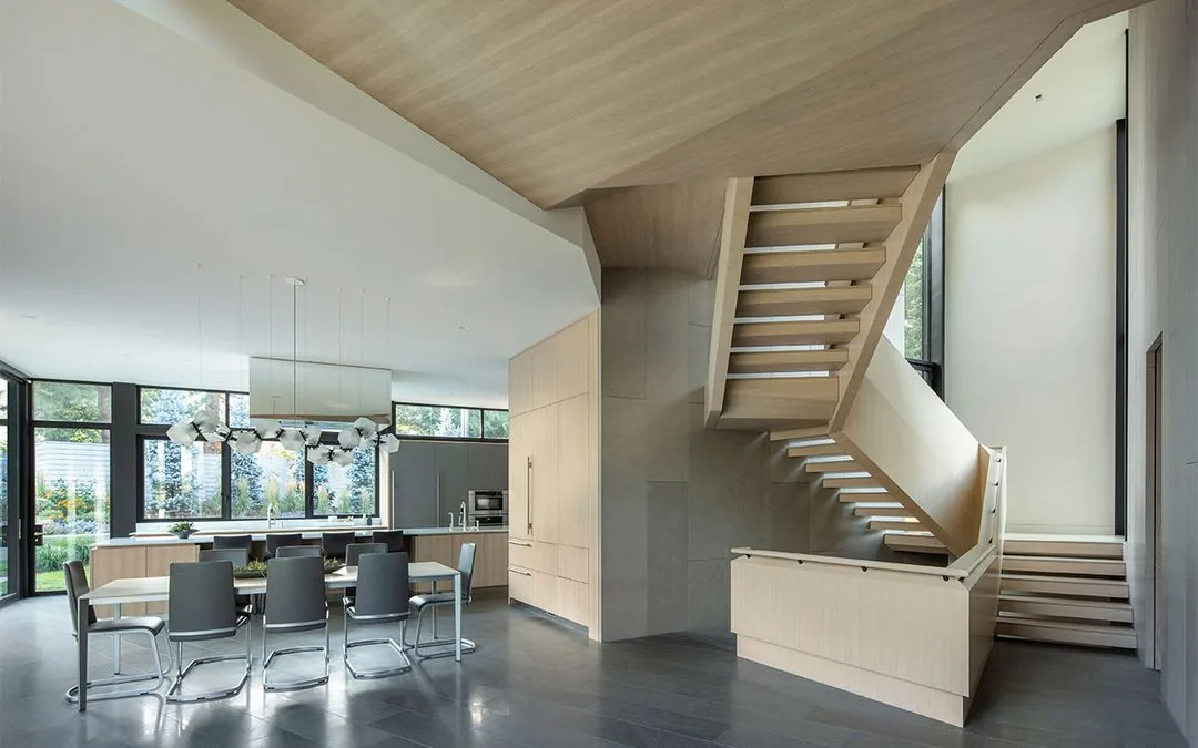 Open-plan kitchen and dining area with floating wooden staircase and expansive windows.
