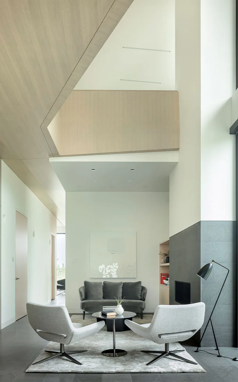 Interior living room featuring modern furniture, a fireplace, and a high ceiling with wood paneling.