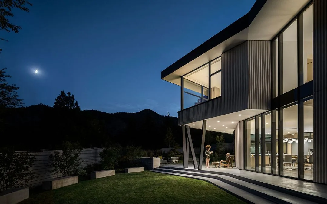 The exterior of Vergence House features a cantilevered upper level with floor-to-ceiling glazing and landscaped lawn under moonlight.