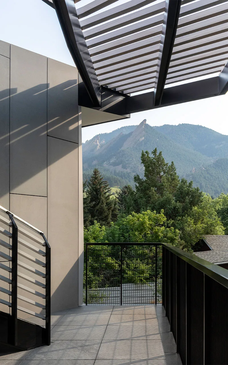Balcony area with metal railing and pergola, showing a mountain landscape beyond.