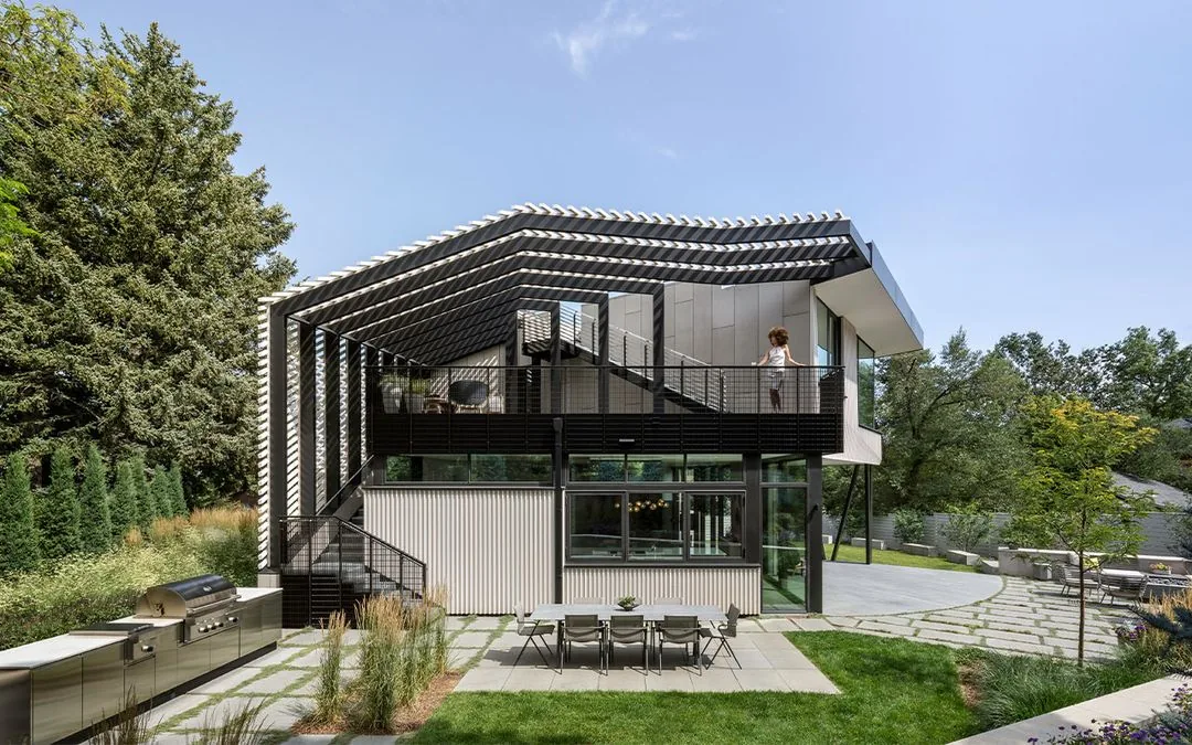 Rear elevation of Vergence House with a large pergola structure, outdoor dining patio, and metal siding finishes.