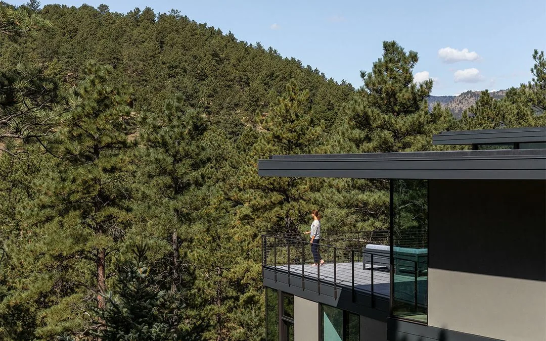 Side view of House 59 with a flat roof and extensive glass walls opening to a balcony surrounded by pine trees.