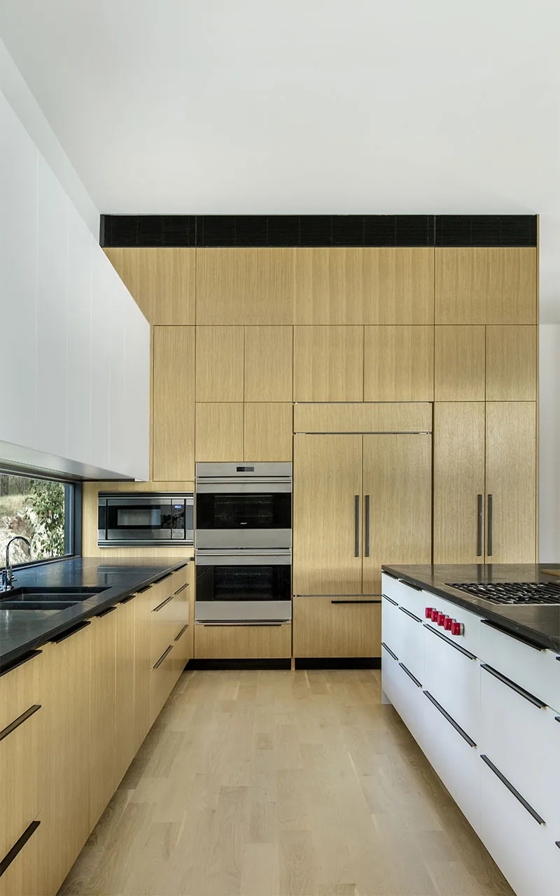 Kitchen featuring wood-paneled cabinets, integrated appliances, and black countertops with a cooktop island.