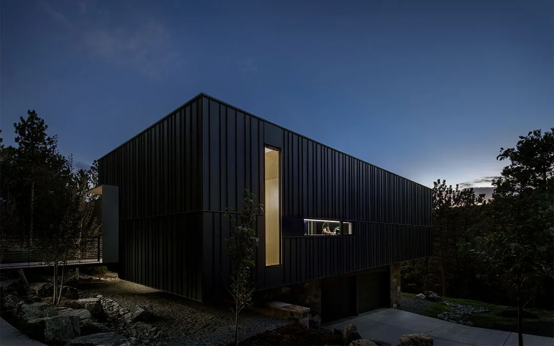 Night exterior view of House 59 showing dark metal cladding and horizontal and vertical window openings.