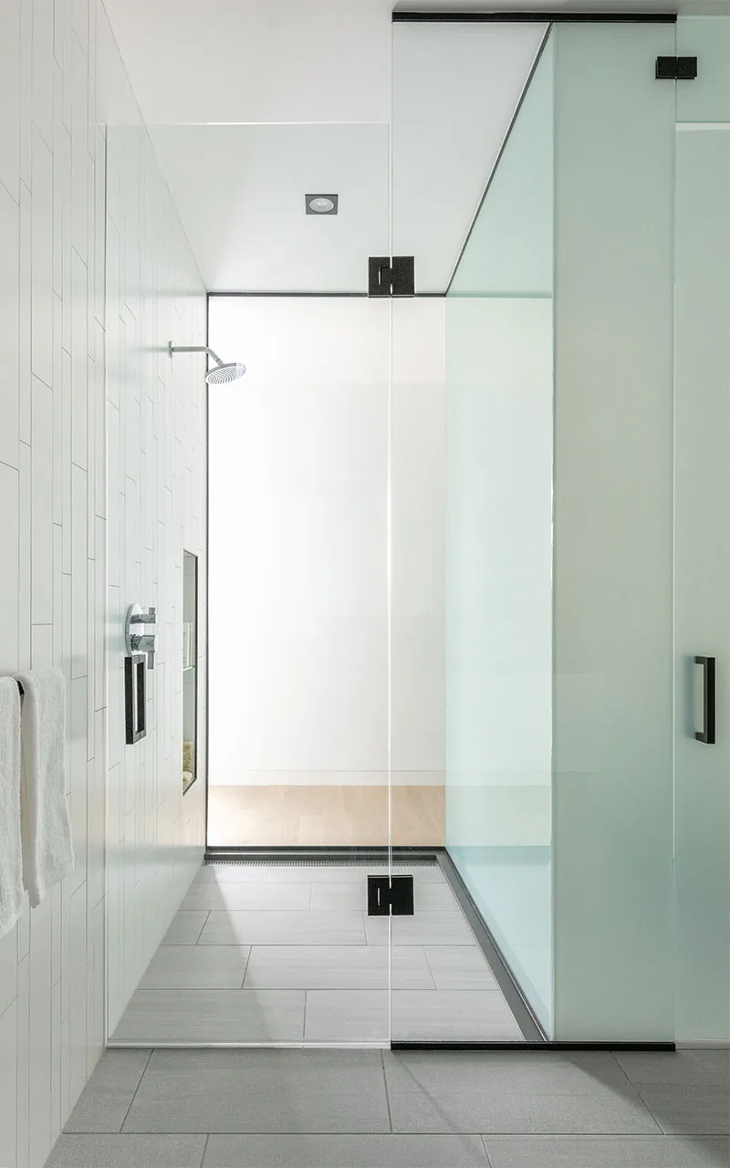 Bathroom shower enclosure with clear glass partition and white vertical rectangular tiles on the wall.