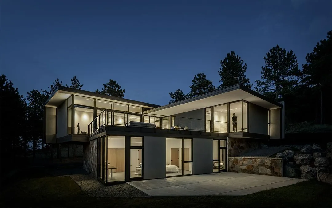 Modern two-story house with extensive floor-to-ceiling glazing and flat roofs illuminated at night.