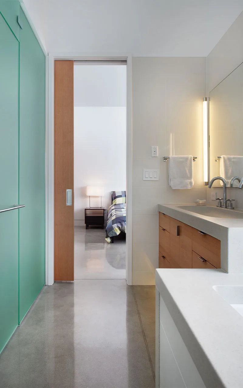 Bathroom with concrete floor and wooden vanity, connected to a bedroom via sliding wooden door.