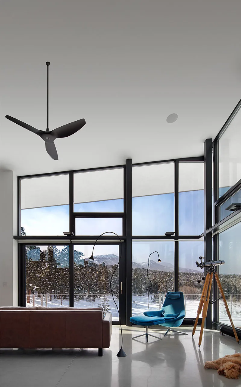 Living room with floor-to-ceiling windows overlooking a snowy forest and mountains, including modern furniture and a telescope.