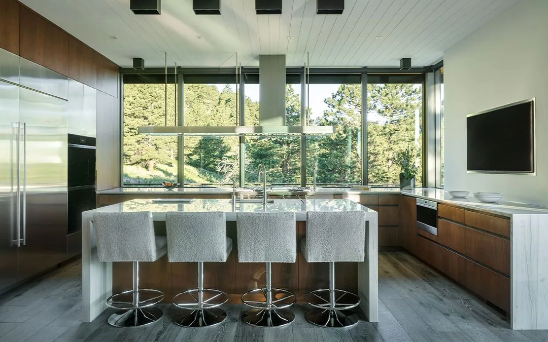 Kitchen with central island and floor-to-ceiling windows overlooking trees.
