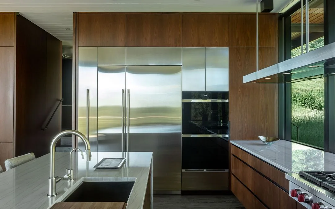 Kitchen featuring stainless steel refrigerator, double oven, wood cabinets, and a marble countertop island with a sink and faucet.