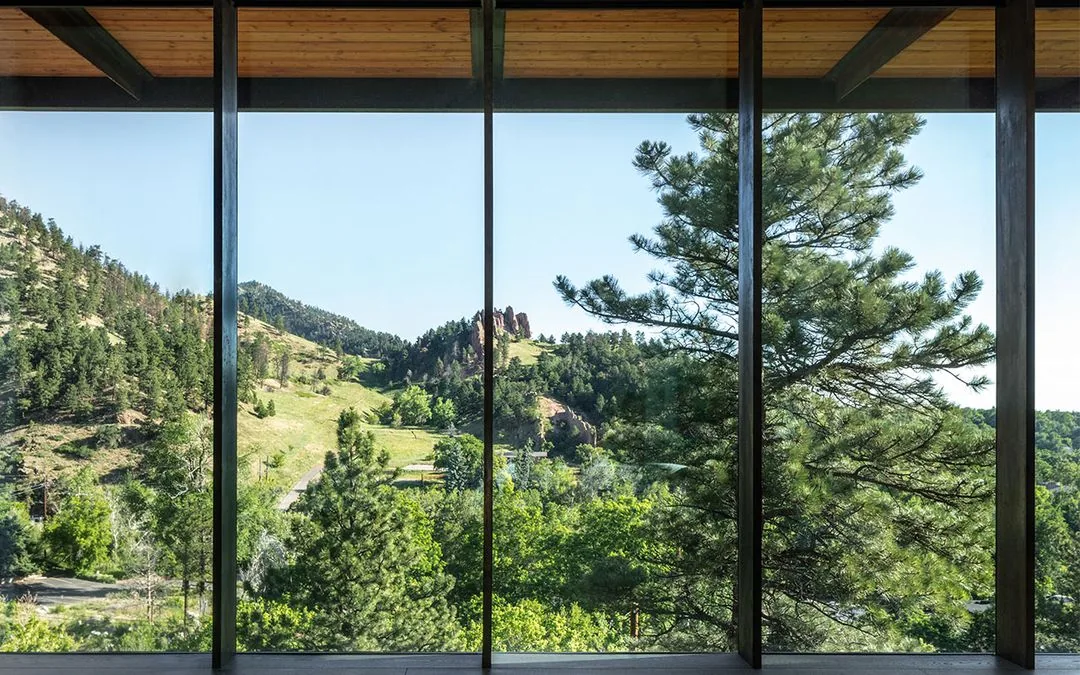 Floor-to-ceiling windows frame a view of a forested hillside and rocky formations.