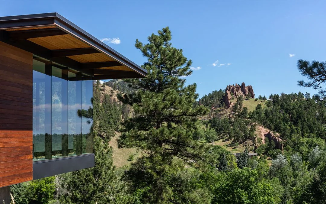 Side exterior of House 306 with floor-to-ceiling windows and wood siding overlooking a forested mountain view.