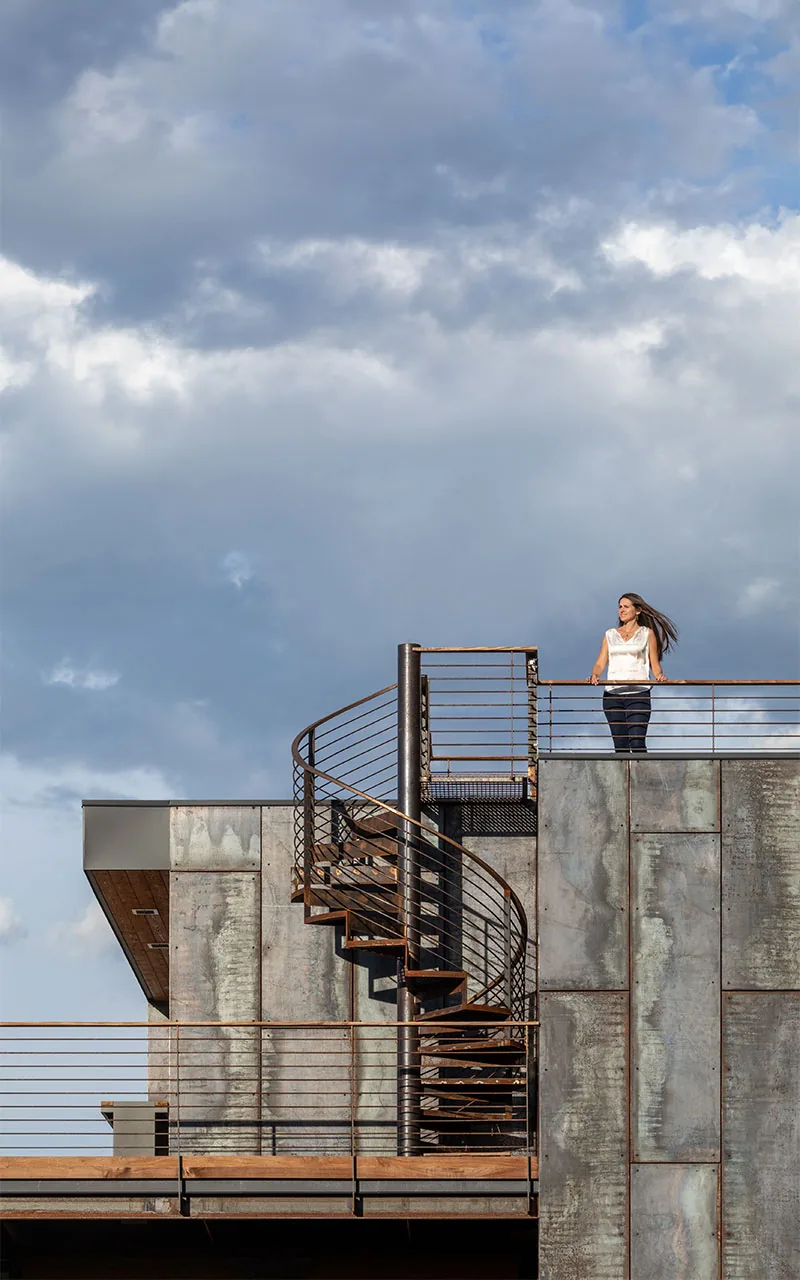 Rooftop terrace with spiral metal staircase and weathered metal panel cladding on facade.