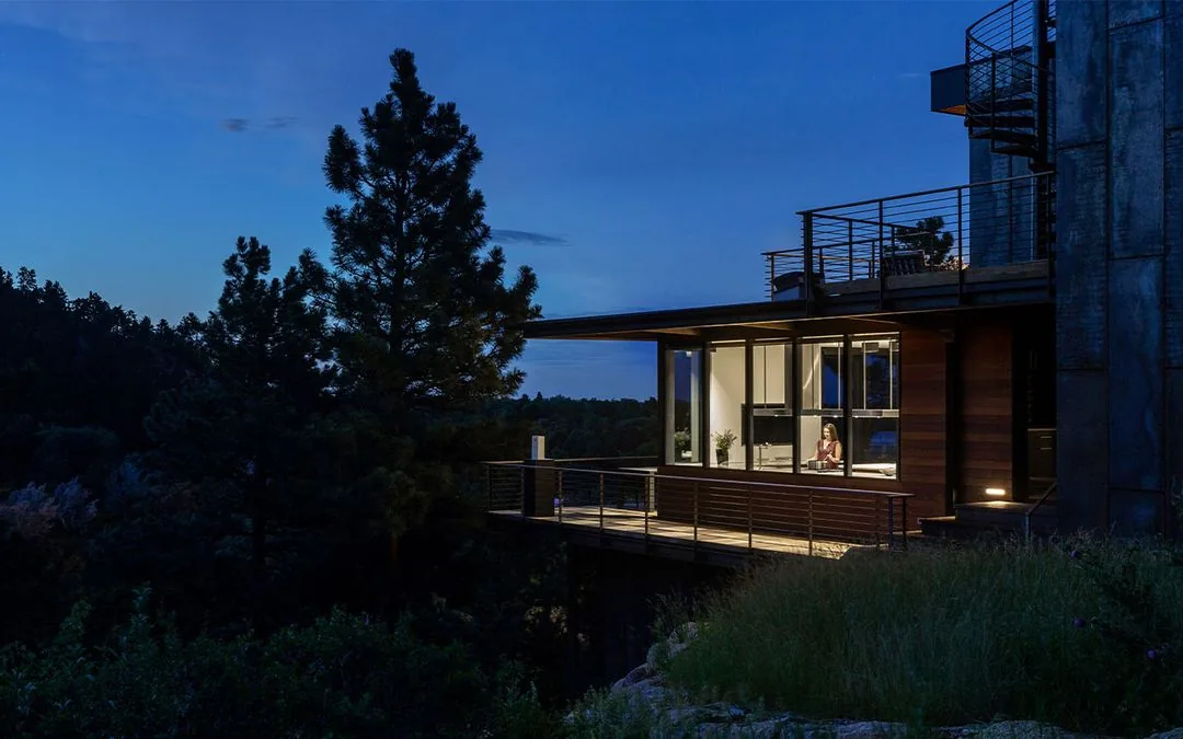 Night exterior view of House 306 showing a cantilevered deck and illuminated interior with large floor-to-ceiling windows.