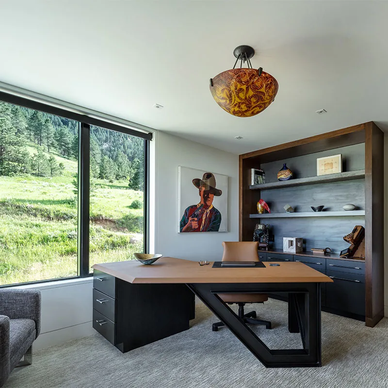 Office space featuring a custom desk and built-in shelving with art pieces next to a large window.