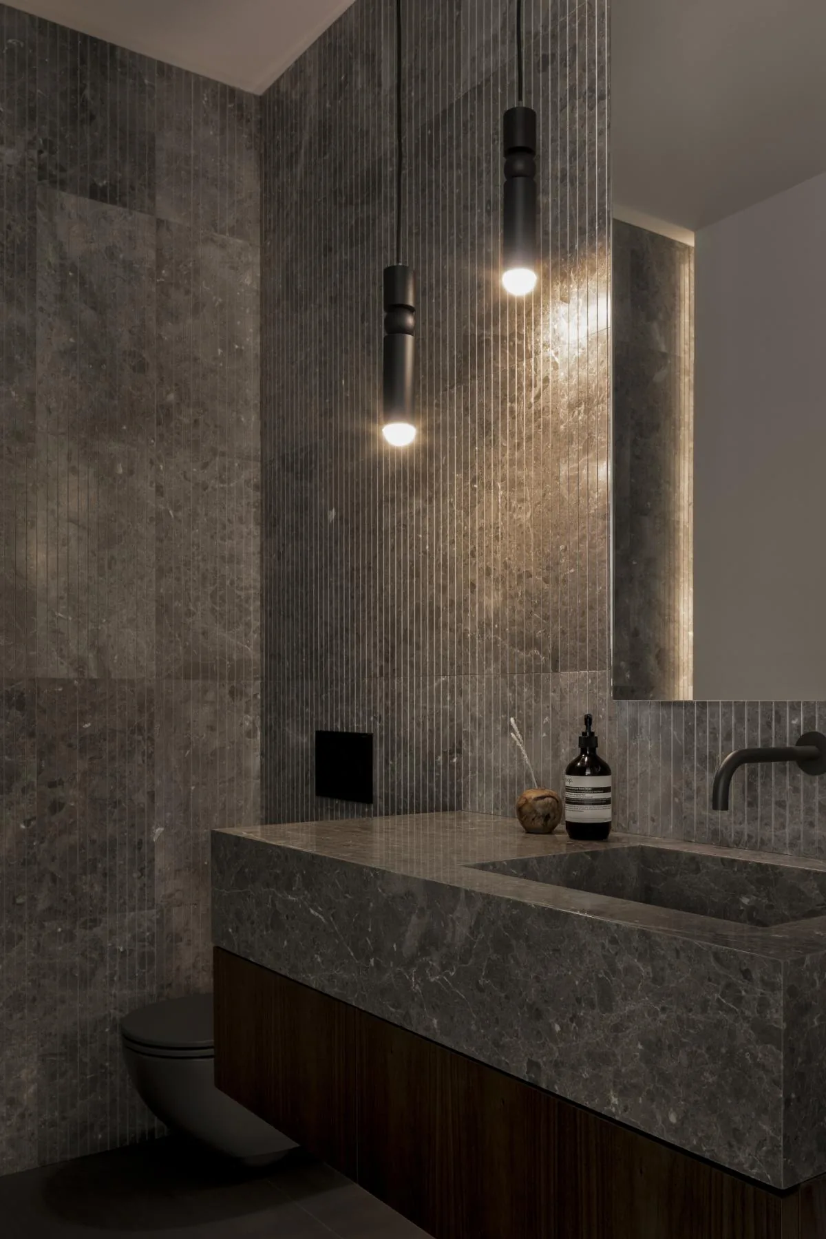 Bathroom featuring dark gray marble walls and countertop with matching integrated sink and pendant lighting.