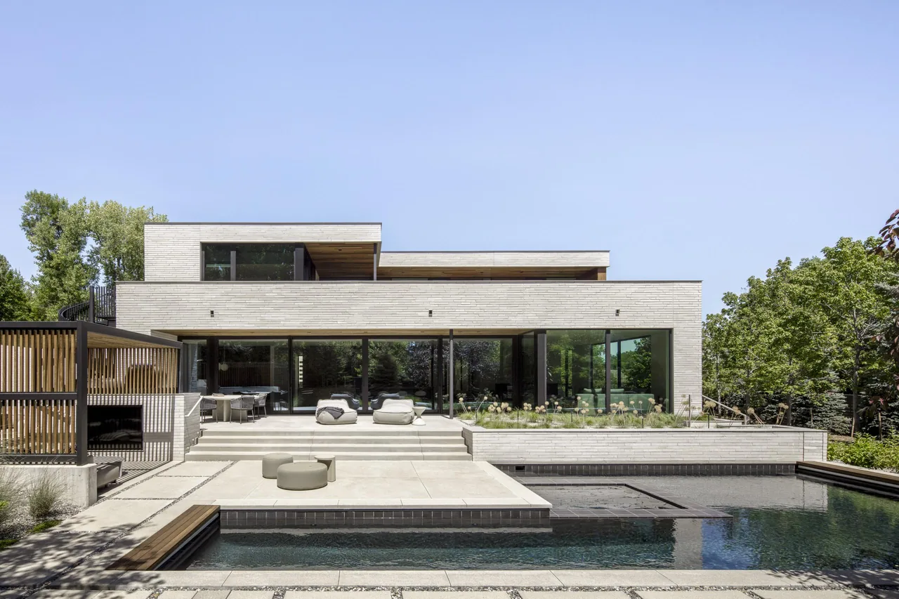 Rear view of a modern villa featuring horizontal light brick cladding and expansive floor-to-ceiling glass sliding doors opening to a pool.