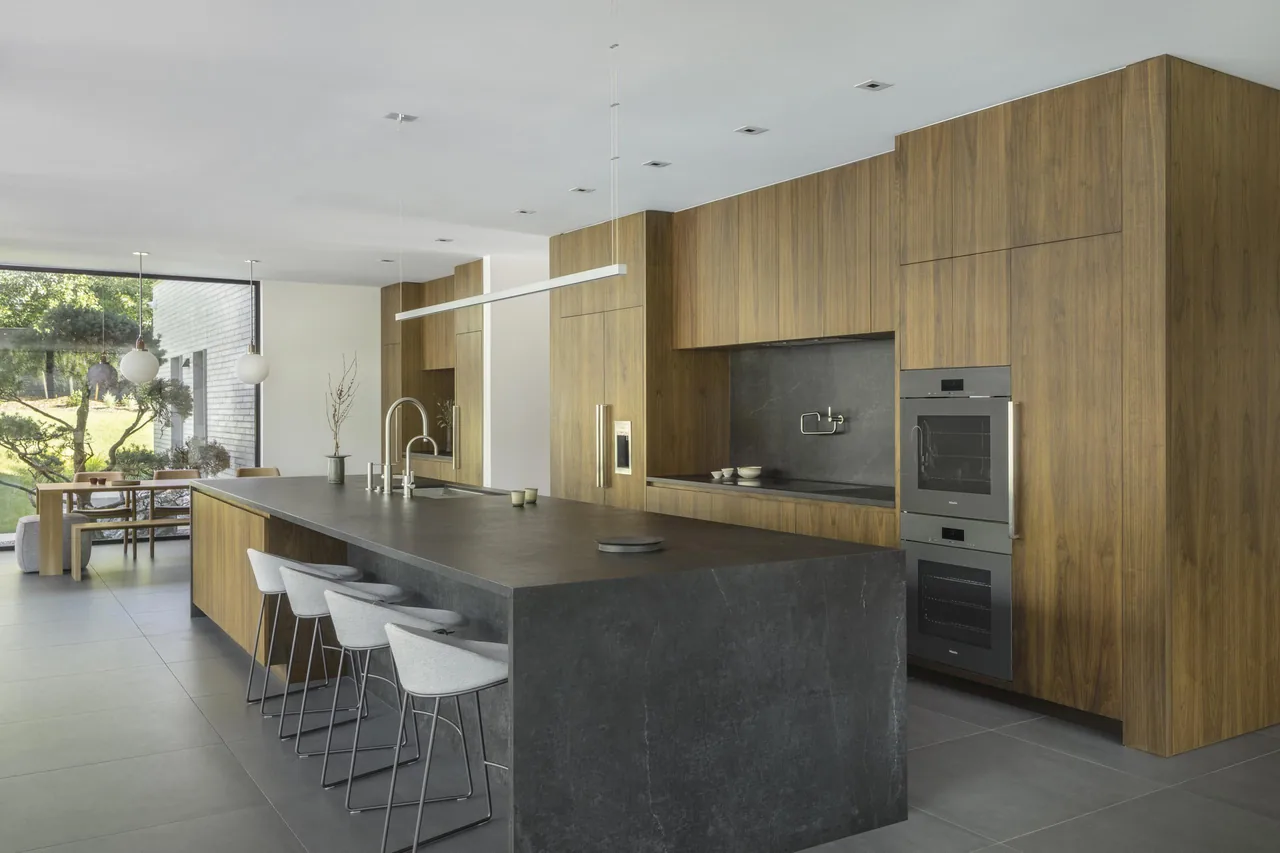 Kitchen with wood-paneled cabinetry, dark stone island, and built-in appliances.