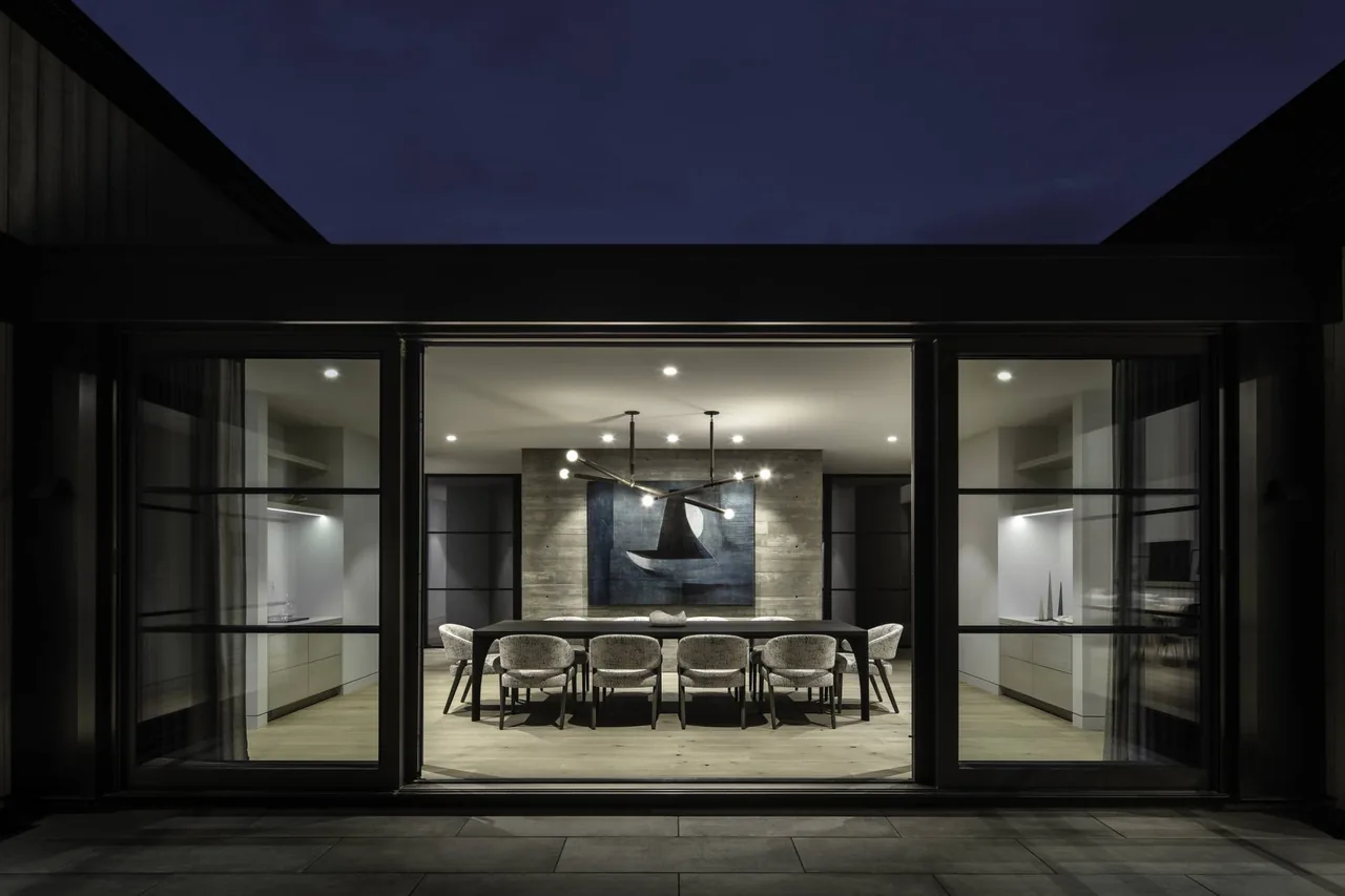 Linden Grove dining room features a long black table, eight upholstered chairs, modern lighting, and a concrete accent wall with art.