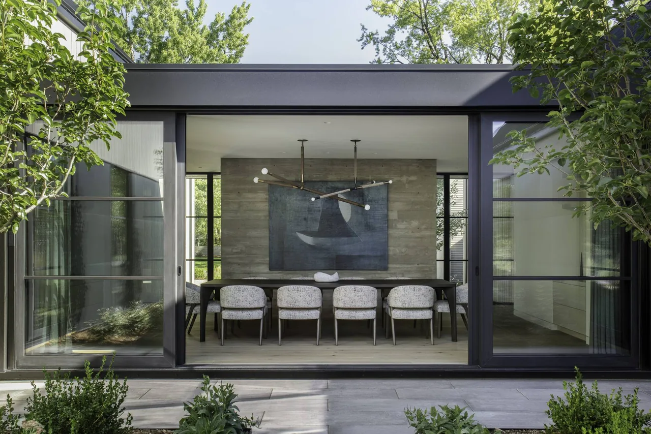 Dining room with floor-to-ceiling sliding glass doors and exposed concrete wall at Linden Grove by Studio B Architects.