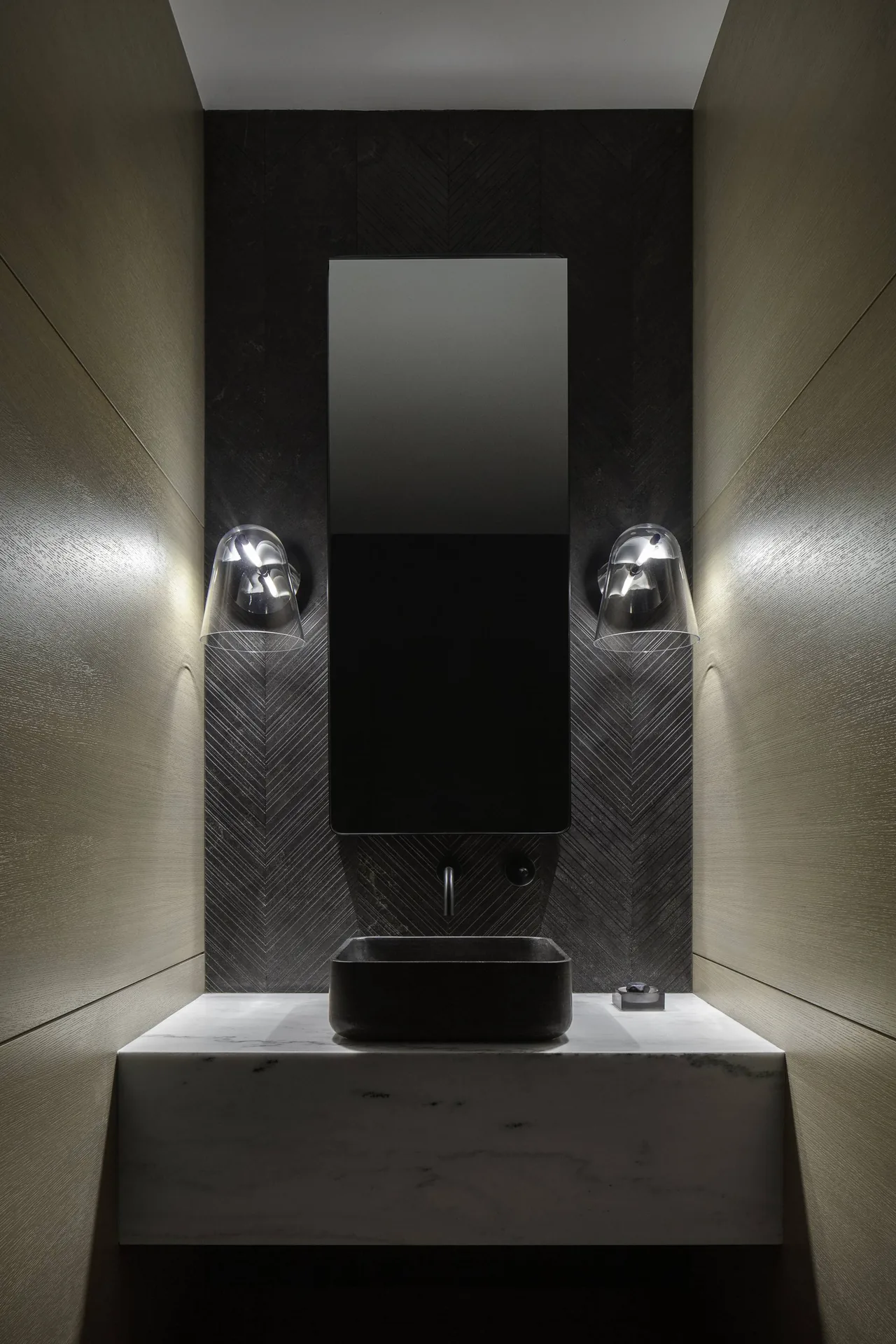 Bathroom vanity with black textured wall, rectangular mirror, glass sconces, black sink, and marble countertop.